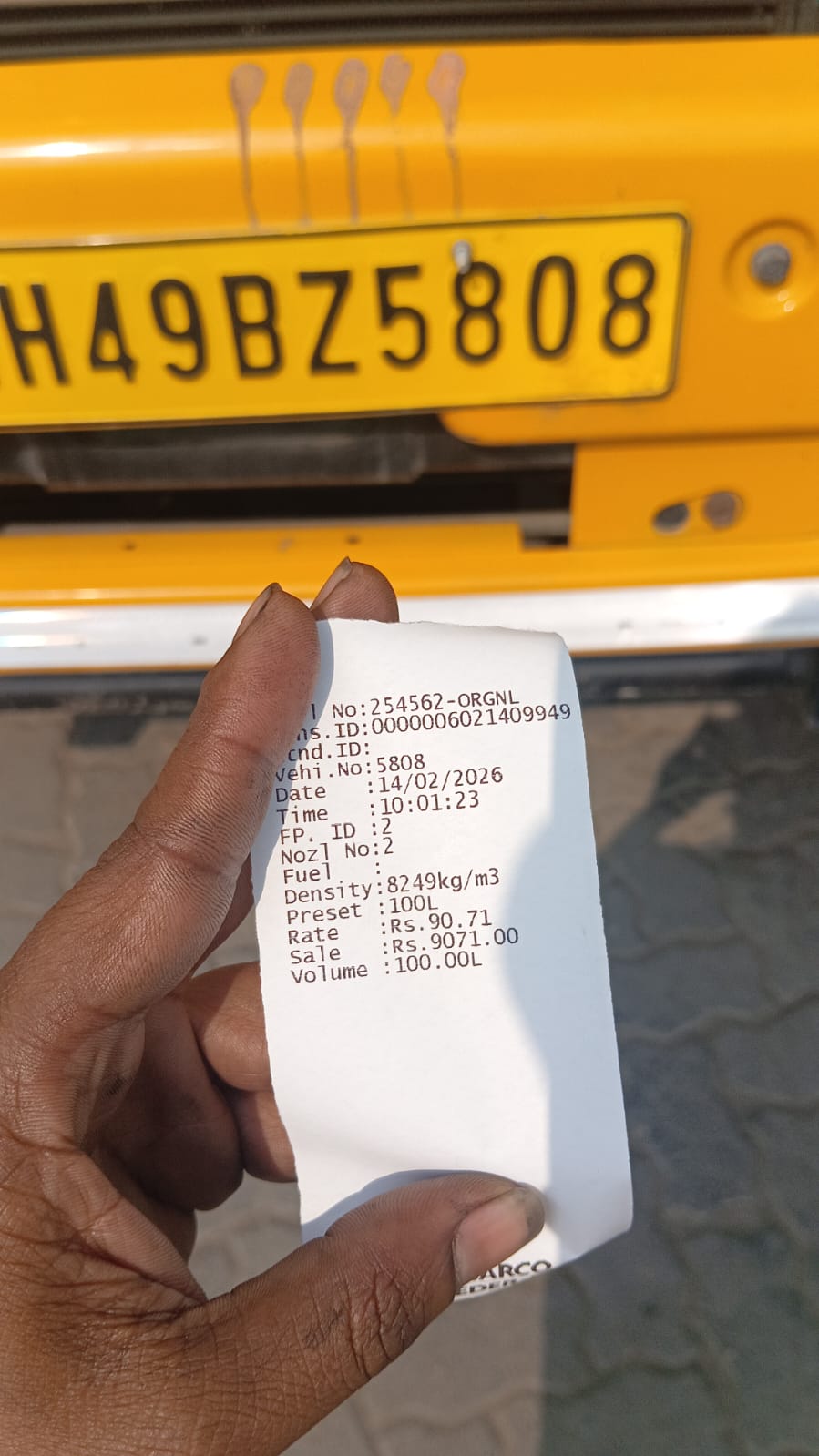 A driver holds a fuel receipt showing 100 liters of diesel at Rs. 90.71 per liter for vehicle 5808, with the yellow truck's license plate visible in the background